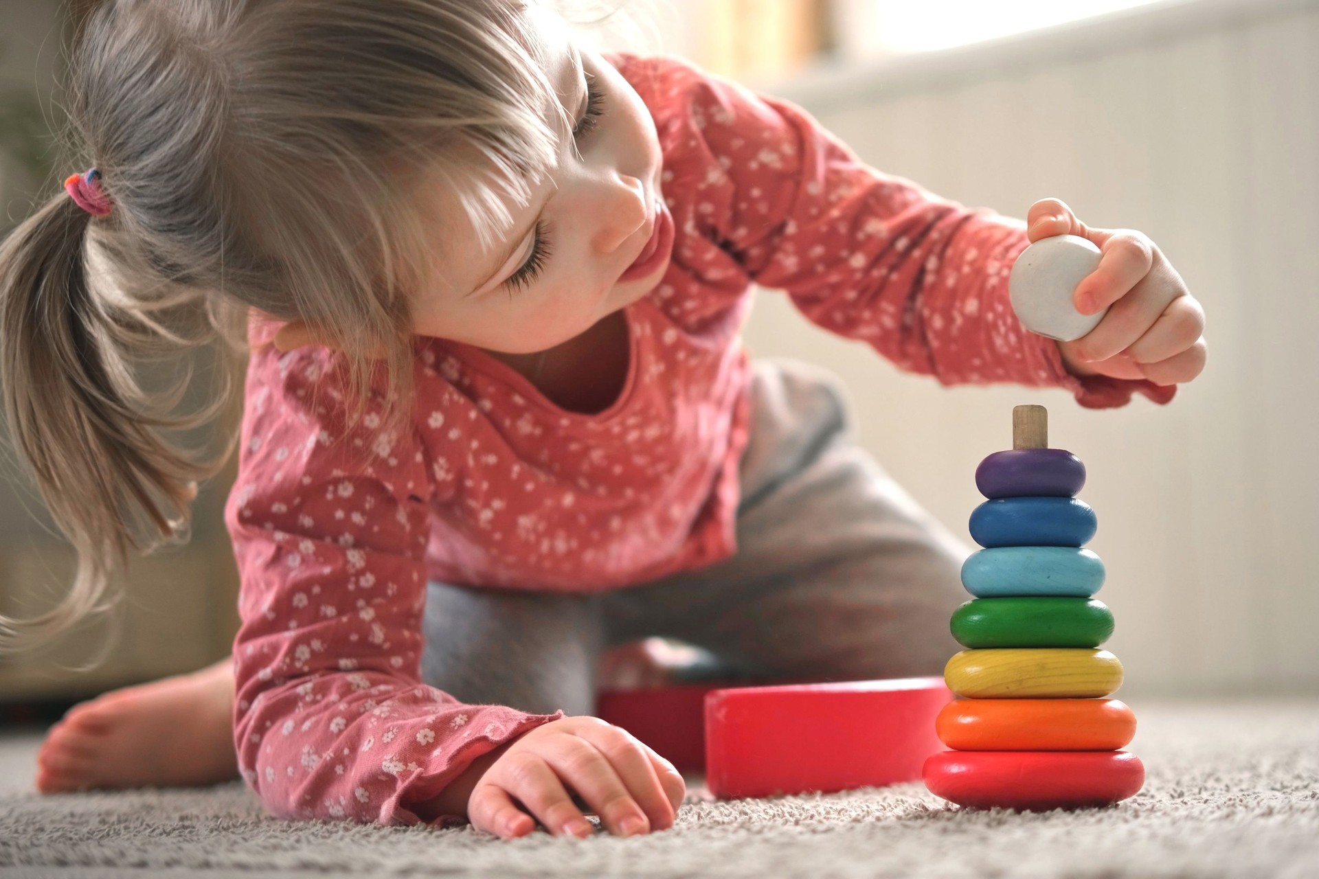 Kid girl play toys at home, kindergarten or nursery. Baby child playing playthings cubes and wood puzzle, pyramid sitting on the floor. Happy preschool education indoor. 3 years old little toddler.