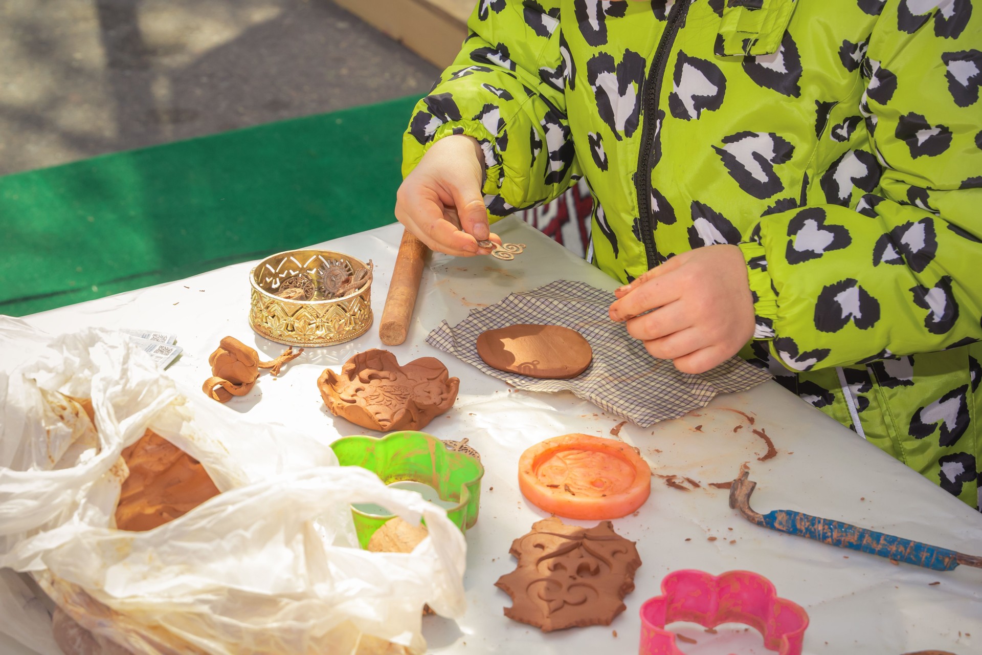 Child makes a plasticine craft with wood details of a traditional Asian ornament outdoors on a sunny day.